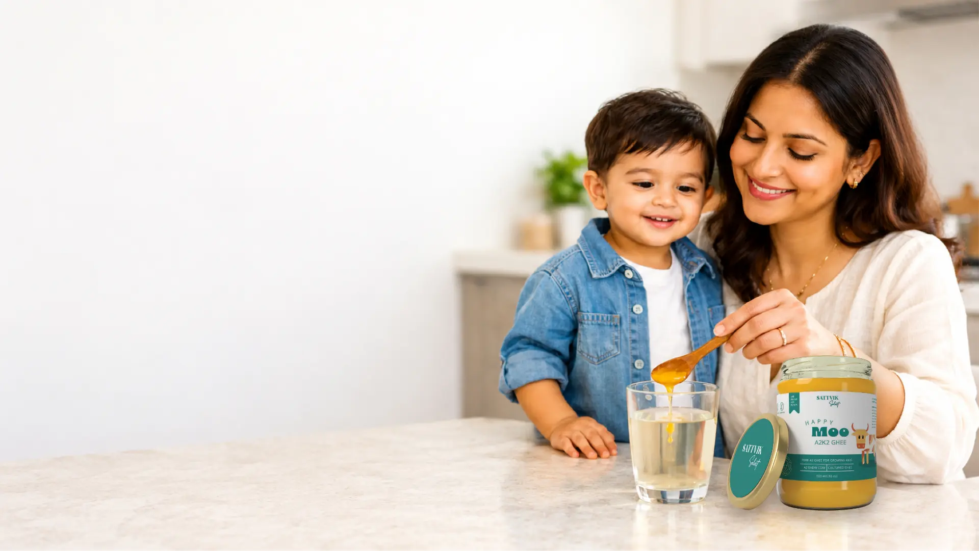A mother giving her child a spoon of Happy Moo A2K2 ghee beside a glass of warm water